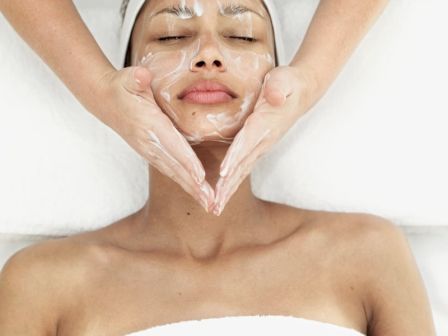 Spa scene: a woman with facial cream mask, hands forming a heart shape around her chin and cheeks.