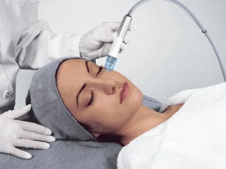 A clinician in gloves injects a syringe near a man&rsquo;s face as he lies on a pillow in a treatment room.