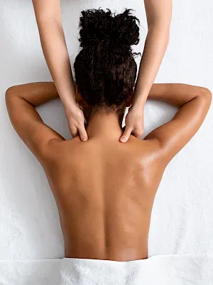 A person lying face down on a massage bed with hands at her shoulders and back exposed.